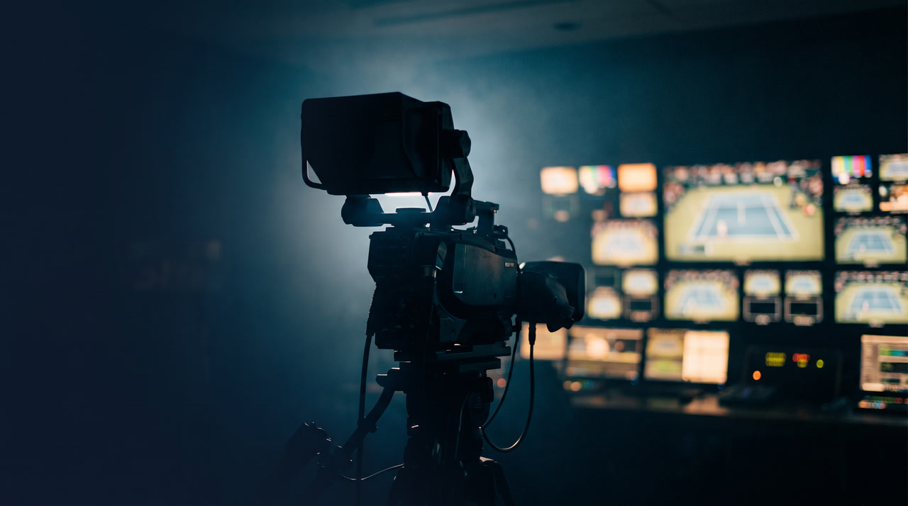 Broadcast camera silhouetted against tennis monitor wall